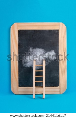 Ladder with a cloud on top, blank chalkboard, blue colored background, copy space, dreaming of success, creative and business concept, achieving new goals
