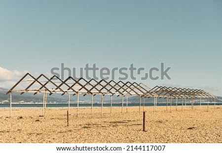 Old canopies from sun on a city pebble beach, Black Sea coast, empty calm  beach on a sunny day.  The sky is burnt out at noon,  sea bay and  in background is Caucasus mountains. Calming pastel swatch