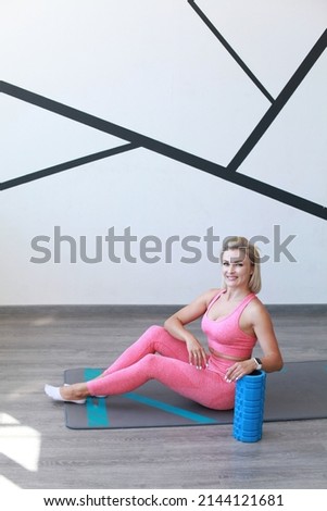 Full-length distance photo amazing fit adult woman doing exercise with foam roller indoors. White wall background. Workout at home and back massage with Myofascial foam roller. 
Equipment for MFR