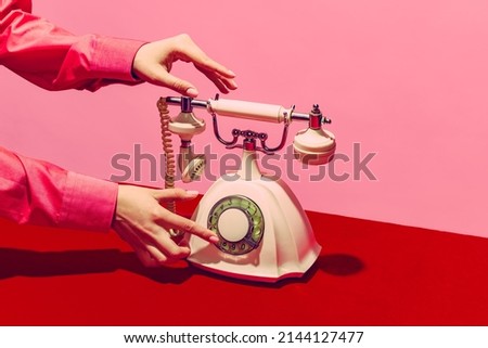 White telephone, Pop art photography. Retro objects, gadgets. Female hand holding handset of vintage phone isolated on pink and red background. Vintage, retro 80s, 70s style. Complementary colors. Royalty-Free Stock Photo #2144127477