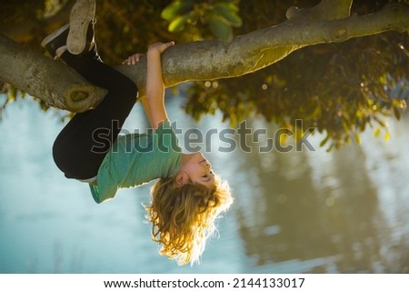 Childhood leisure, happy kids climbing up tree and having fun in summer park. Young boy playing and climbing a tree and hanging upside down. Teen boy playing in a park. Royalty-Free Stock Photo #2144133017