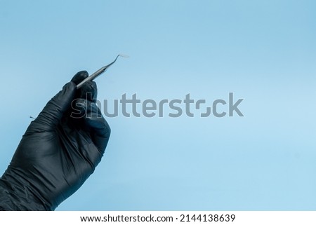 Cropped shot of professional dentist in black medical gloves with dental tool. Dental concept. Isolated on blue background