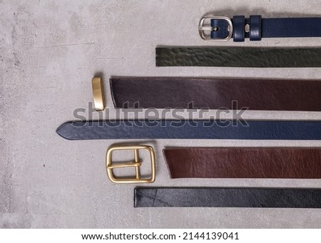 close up of leather belts on gray background. Ends of smooth leather belts with classic buckle.
