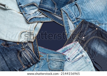 Various blue jeans pants or trousers made of blue-colored denim cloth. Closeup abstract texture cotton fabric for background design. Pair of jeans, pockets, rivets, buttons, seams with selective focus Royalty-Free Stock Photo #2144156965