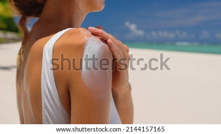 Close up of a happy smiling young woman is applying a sunscreen or sun tanning lotion on a shoulder to take care of her skin on a seaside beach during holidays vacation. Royalty-Free Stock Photo #2144157165
