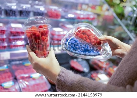 A woman's hand picks fresh berries and raspberries at the supermarket. Wide choice of fresh, organic and healthy products