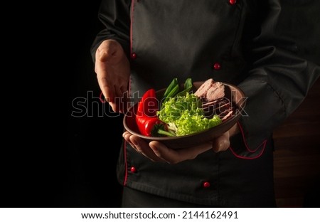 In the chef hand is a plate with chopped steak and vegetables. The concept of cooking on a dark background. Asian cuisine.