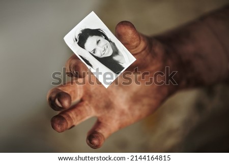 Where is she now. A dirty hand holding a black and white picture of a beautiful woman.