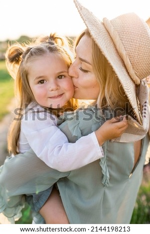 A young mother in a straw hat kisses her little daughter