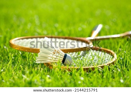Two badminton rackets and a shuttlecock lie on the green grass. Outdoor recreation and fresh air. The sun's rays. Lawn for playing badminton. Royalty-Free Stock Photo #2144215791