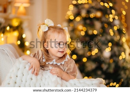 a cheerful cute little girl with two ponytails on a chair in a room decorated for the New Year. happy childhood. the tradition of celebrating Christmas and giving gifts.