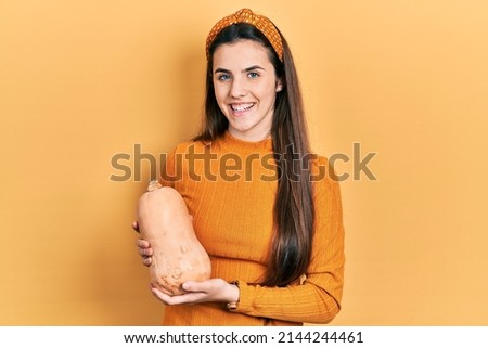 Young brunette teenager holding healthy fresh pumpkin looking positive and happy standing and smiling with a confident smile showing teeth 