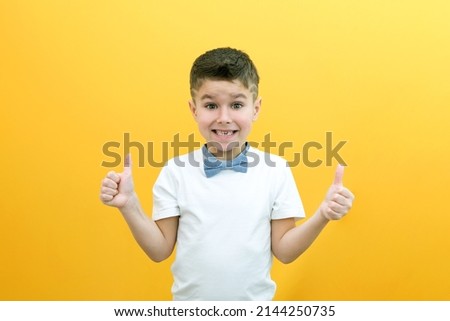 Cheerful excited boy in white shirt with bow tie posing standing, showing like on copy space mockup isolated on bright yellow wall background studio portrait