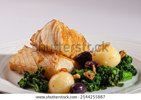 Grilled cod fish served with broccoli, black olives and roasted potatoes, drizzled in olive oil.