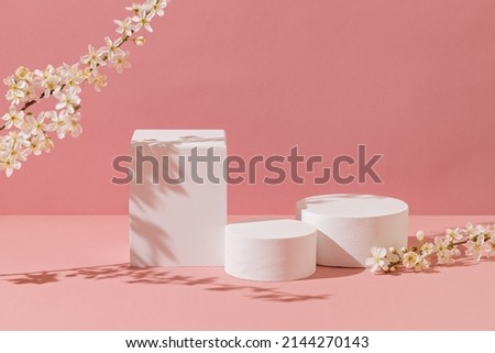Empty white podiums with flowers on pastel pink background. Minimal geometric podium. Mockup.