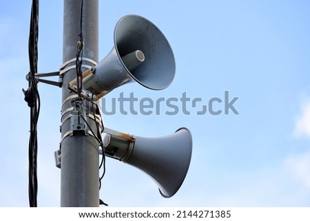 Loudspeakers on pole, alarm siren in city. Two public address system speakers on blue sky background Royalty-Free Stock Photo #2144271385