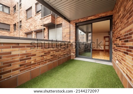 Enclosed terrace with glass and metal, brown bricks and green artificial grass floor in urban residential housing Royalty-Free Stock Photo #2144272097