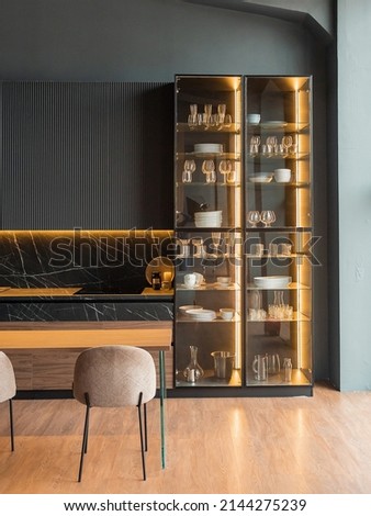 contemporary kitchen in a modern style, wooden floor, dark grey interior.  kitchen island. cabinet with glass doors and lighting for wine glasses. upholstered chairs. countertops with black cabinets