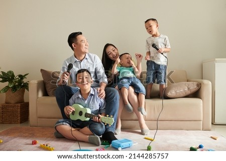 Happy Asian family of five laughing, playing ukulele and singing song into microphone Royalty-Free Stock Photo #2144285757