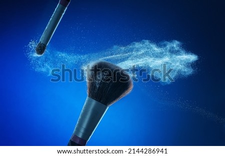Make-up brush with white powder splashes explosion on blue background. Beauty concept.