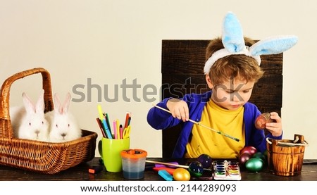 Child boy in bunny ears decorate Easter eggs. Childrens creativity. Decorating eggs. Spring holiday.
