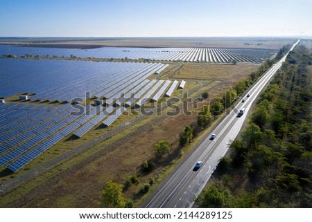 Aerial view of a solar power plant from a variety of photovoltaic panels. Next to the power plant there is a road going beyond the horizon. Shooting from a drone.