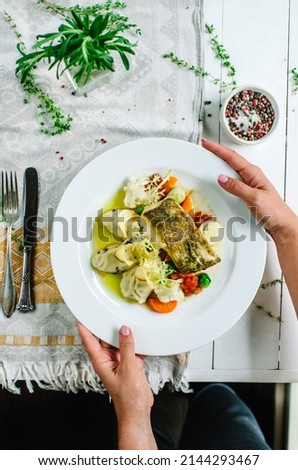 White fish with herbal oil. Mashed potatoes with olives and mixed vegetables - cauliflower, carrots, tomatoes and Brussels sprouts. A woman holds a plate in her hands. Photo in rustic style.