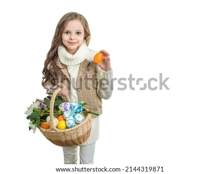 Smiling little cute girl with basket full of colorful easter eggs and flowers holds easter egg in hand. Easter concept. Spring season.
