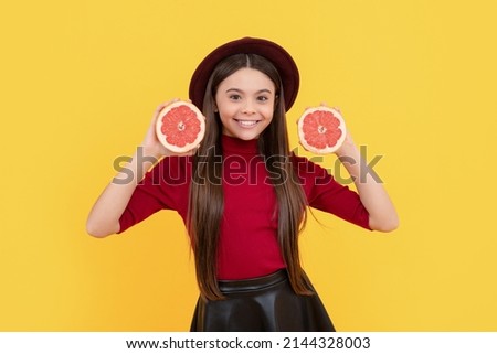 positive child in hat with grapefruit and book on yellow background, skincare