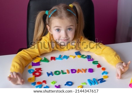 the concept of holidays, the child has English letters laid out on the table, the word holidays is written, waiting for a break from studying