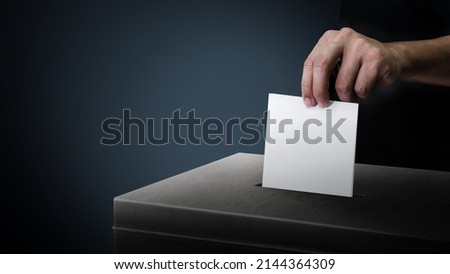 Dark side ballot box with hand person vote on blank voting slip at dark background. Royalty-Free Stock Photo #2144364309