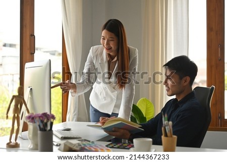 A portrait of happy Asian businesspeople working together on a document and pointing on a computer in the office, for business and technology concept.