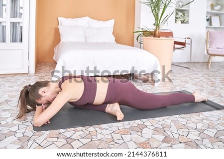 Young woman going yoga exercise at home. Health care online lessons. Pigeon Indoor fitness workout. Remote sport trainer. Morning activity. Floor pilates mat. Female person lifestyle. Asana pose Royalty-Free Stock Photo #2144376811