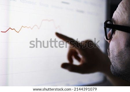 A businessman is looking at a graph on a monitor. An exchange broker evaluates stock market trends. A man with glasses in front of a curve of the dynamics of economy. Royalty-Free Stock Photo #2144391079