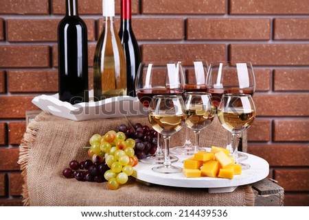 Bottles and glasses of wine, cheese and ripe grapes on table on brick wall background