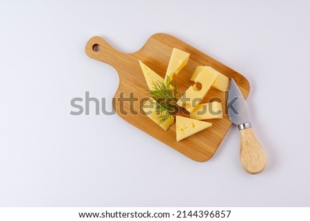 triangular piece of yellow cow's milk swiss cheese with holes cutout on cutting board, isolated white background Royalty-Free Stock Photo #2144396857