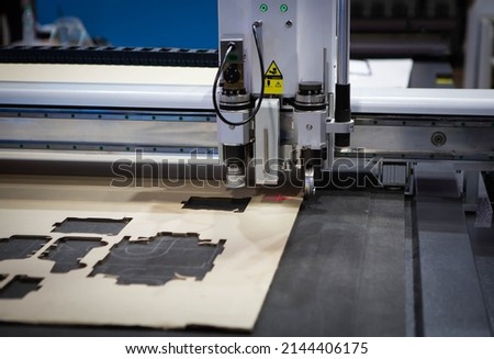 Digital die cutter machine cutting corrugated cardboard box for packaging. Industrial manufacture. Royalty-Free Stock Photo #2144406175