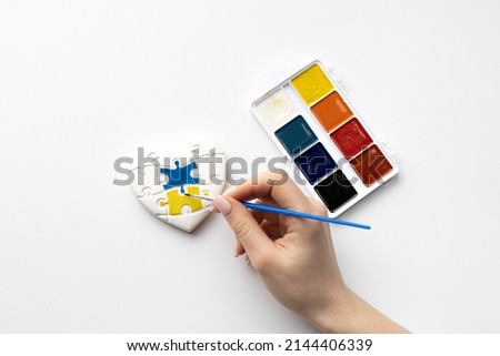 Woman's hand paints a watercolor heart in the form of puzzles with the colors of the flag of Ukraine