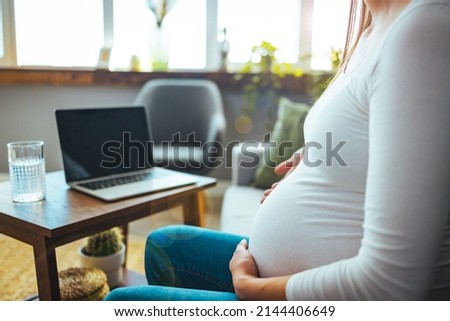 Future attractive cheerful mum sitting in chair in bright light flat and using pc laptop while speaking with intelligent doctor about pregnancy. Cropped view of pregnant patient having consultation