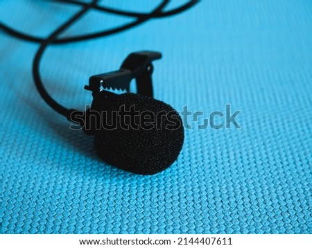 Lavalier microphone on a blue background, close-up. A lavalier microphone or lavalier is a small microphone used for television, theater, and public speaking.