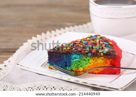 Delicious rainbow cake on plate and cup with hot drink, on wooden background