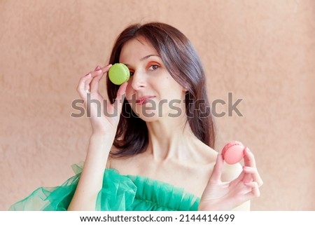 Brunette woman with bright make up holds colorful french macarons. Creative National Macaroon Day concept. Vibrant summer photography.