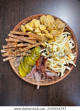 large vertical photo. homemade food. a large clay plate with various snacks for alcoholic drinks, beer. dried fish, smoked cheese and seasoned croutons on the table. anti-diet. harmful products.