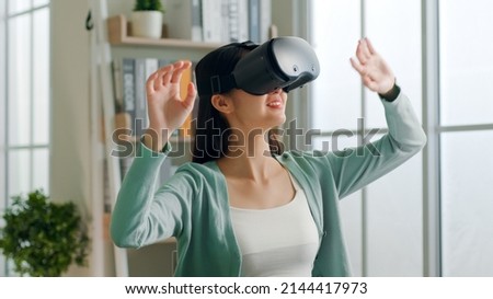 Young Asian woman feeling excited while using 360 VR headset for virtual reality, metaverse at home 