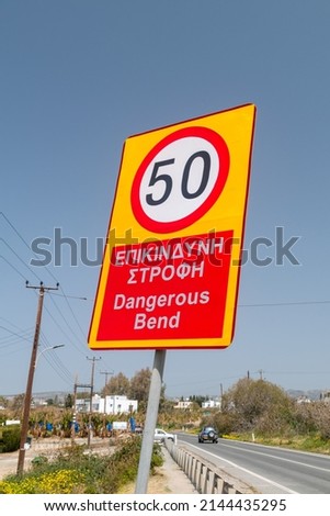 Dangerous bend warning and reduce speed sign. Reduce speed inscription in English and Greek languages.