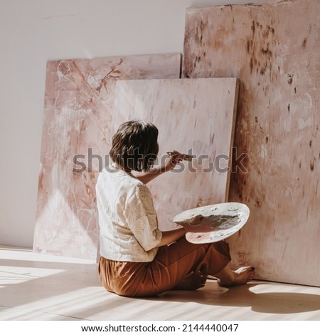 Young woman artist painting abstract picture in studio with sun light. Aesthetic minimalist art work creation concept