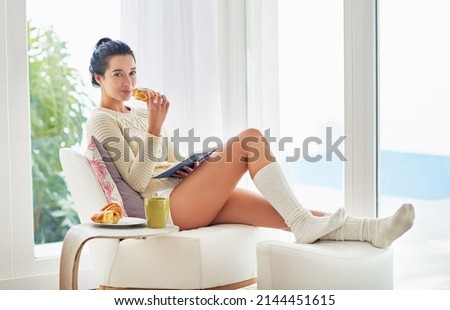Me time is reading time. Portrait of young woman relaxing with a book and a snack at home. Royalty-Free Stock Photo #2144451615