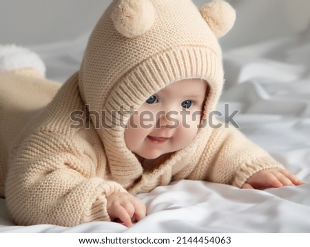 Just beautiful. Cute smiling baby. Cute 3 month old Baby girl infant on a bed on her belly with head up looking with her big eyes. Warm, fluffy biege clothes. Closeup. Three months old baby Royalty-Free Stock Photo #2144454063