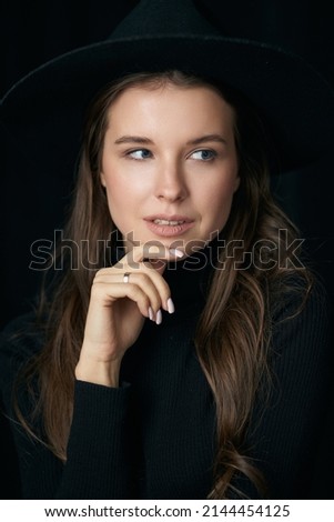 Brown haired lady model with expressive look in black sweater posing on black background in studio closeup