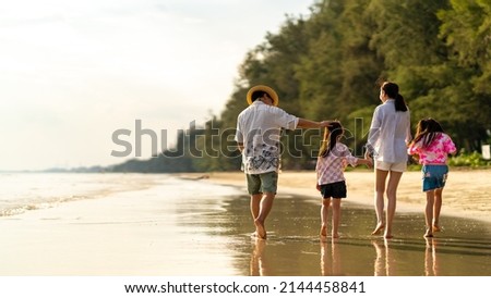 Happy Asian family father and mother with two little daughter walking and playing together on the beach at summer sunset. Parents with child girl kid enjoy and fun outdoor lifestyle on summer vacation